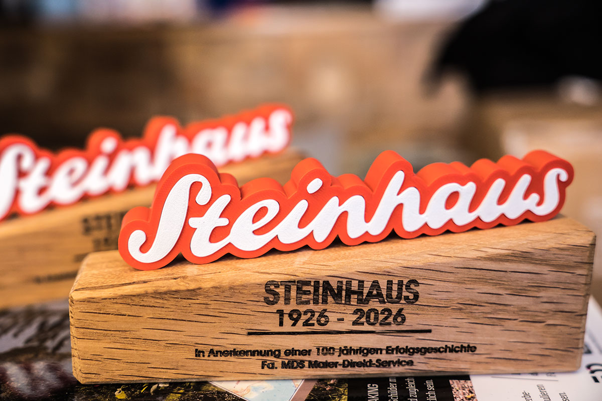 Auszeichnung für Fa. Steinhaus in Lennep. Rotes §D Druck Teil mit weißen Einlegern auf einem Holzsockel mit Gravur